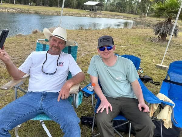 Two men are sitting in chairs in front of a lake.