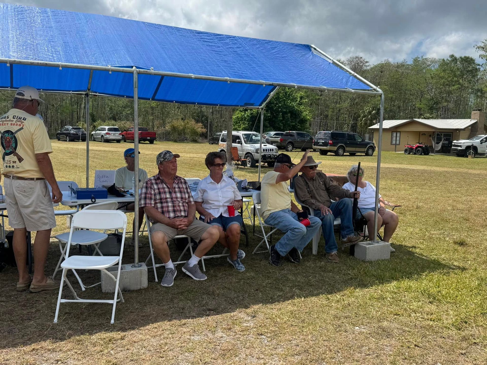 A group of people are sitting under a blue tent in a field.