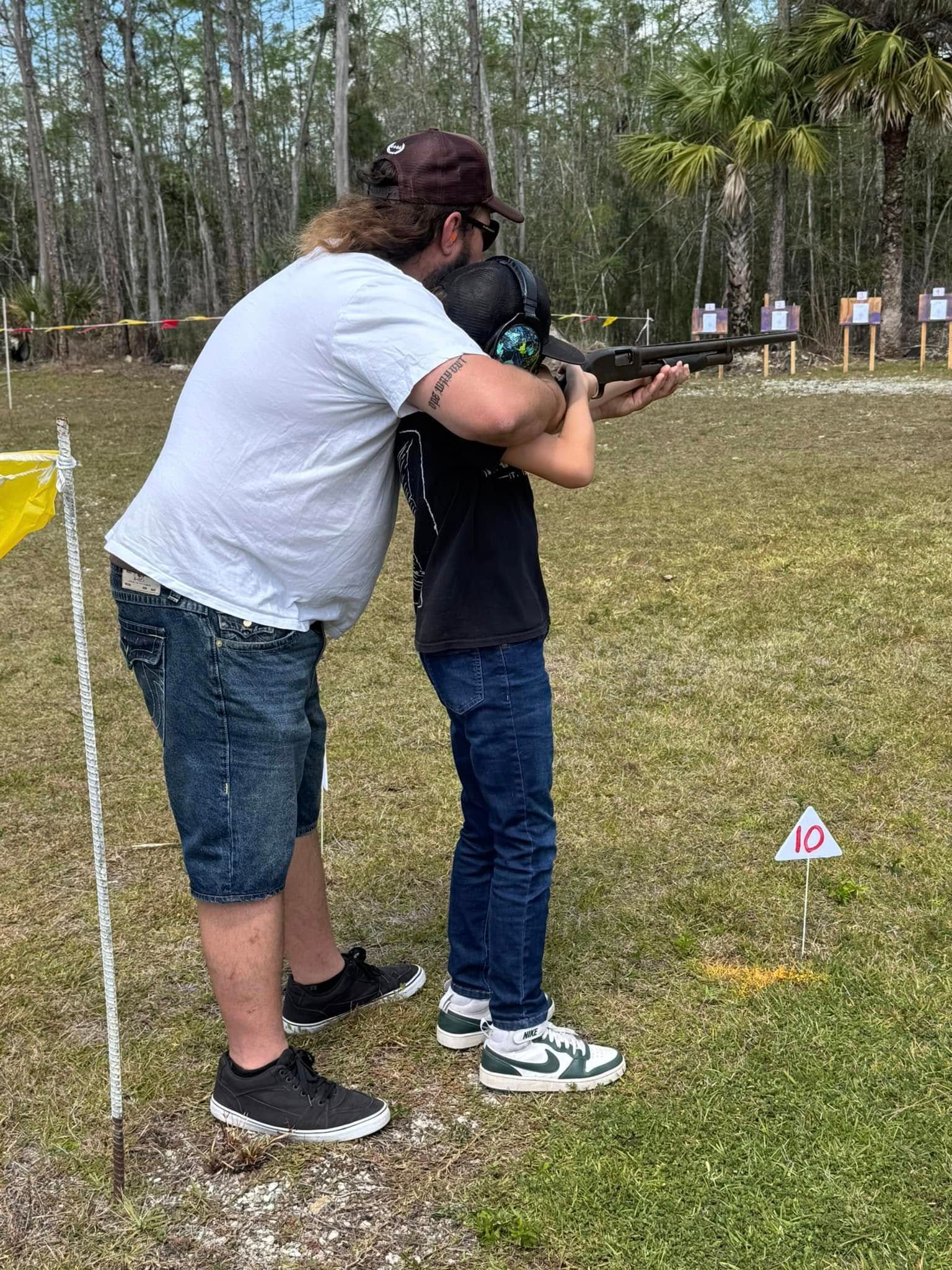 child shooting a gun with help from an adult