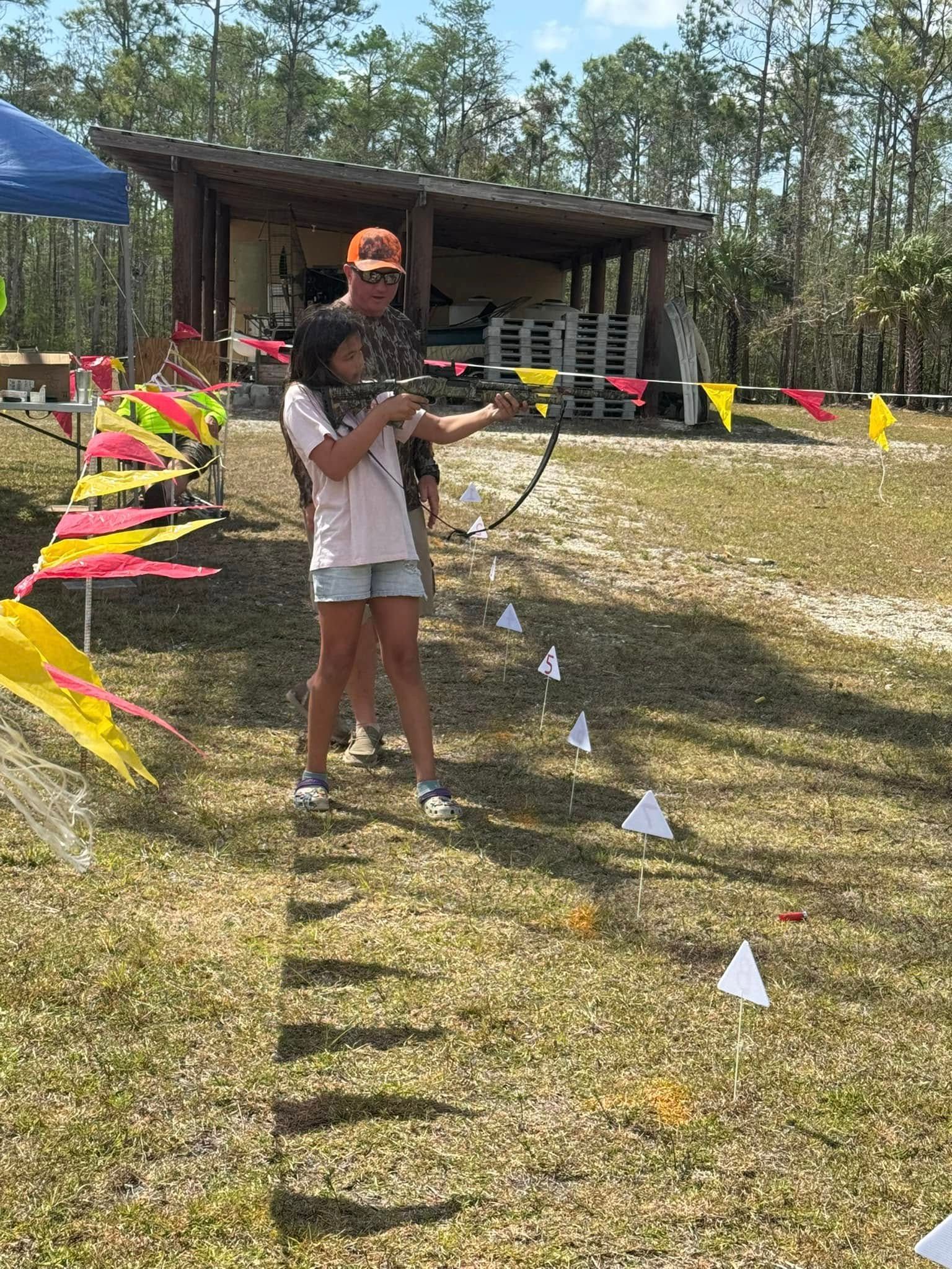 A man and a girl are playing archery in a field.