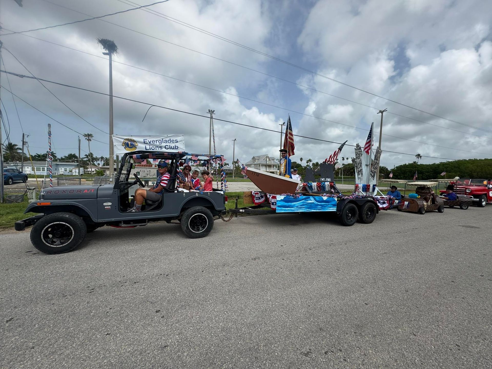 Gray Jeep pulling a parade float with a boat display on a sunny day.