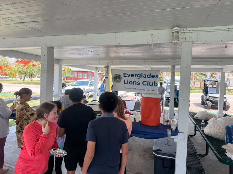 People at a Lions Club event under a shelter, serving food and drinks outdoors.