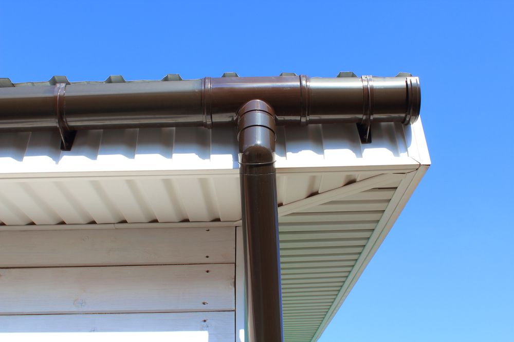Brown gutter and downspout on a white house under a clear blue sky.