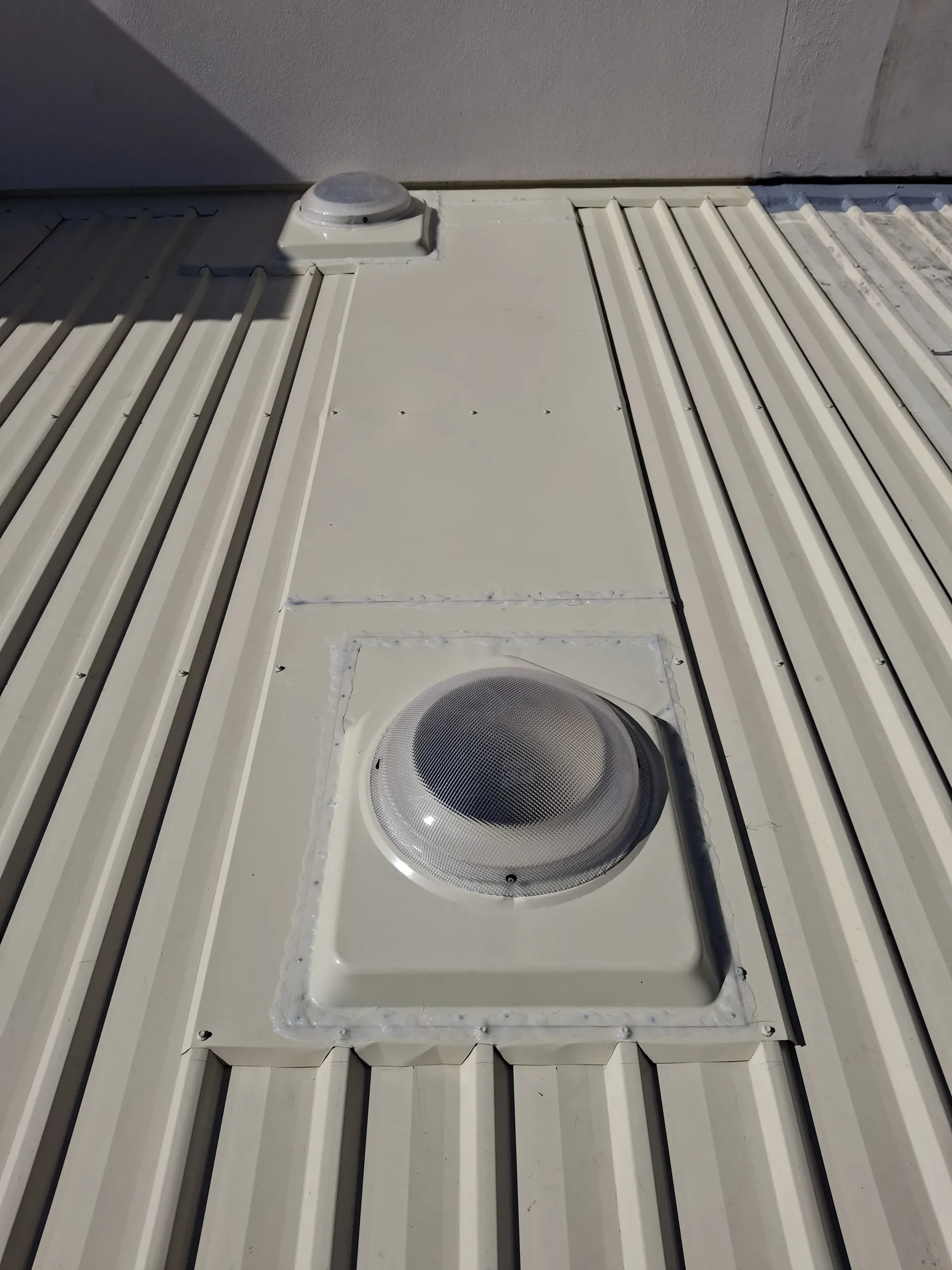 Skylight on a white metal roof, with a clear dome. A white drainpipe and wires are also visible.