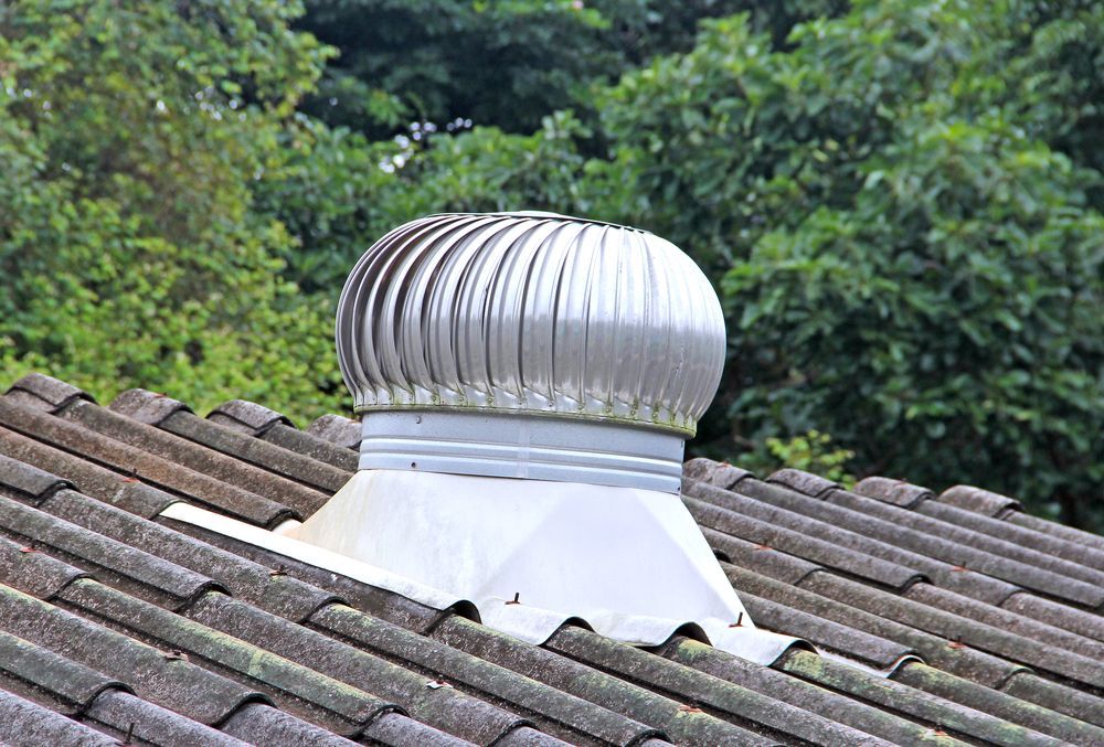 Metallic roof vent on a tile roof, with green foliage in the background.