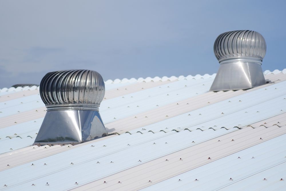 Two rotating roof vents on a white and silver corrugated metal roof against a pale blue sky.