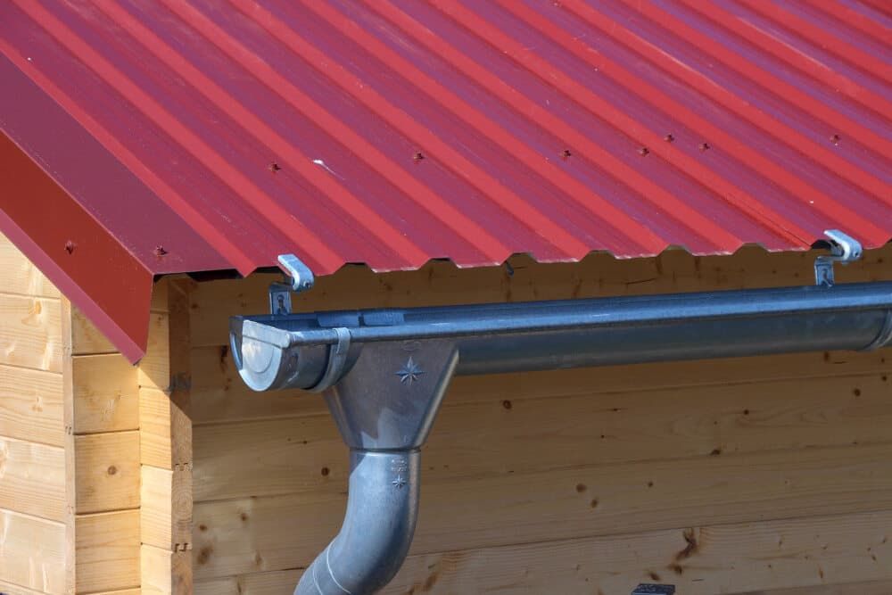 Red corrugated metal roof with silver gutters on a wooden building.