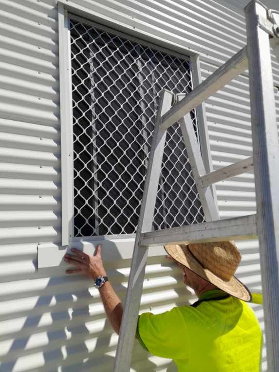 Exterior view of a weathered white building with a corrugated metal roof, against a cloudy sky.