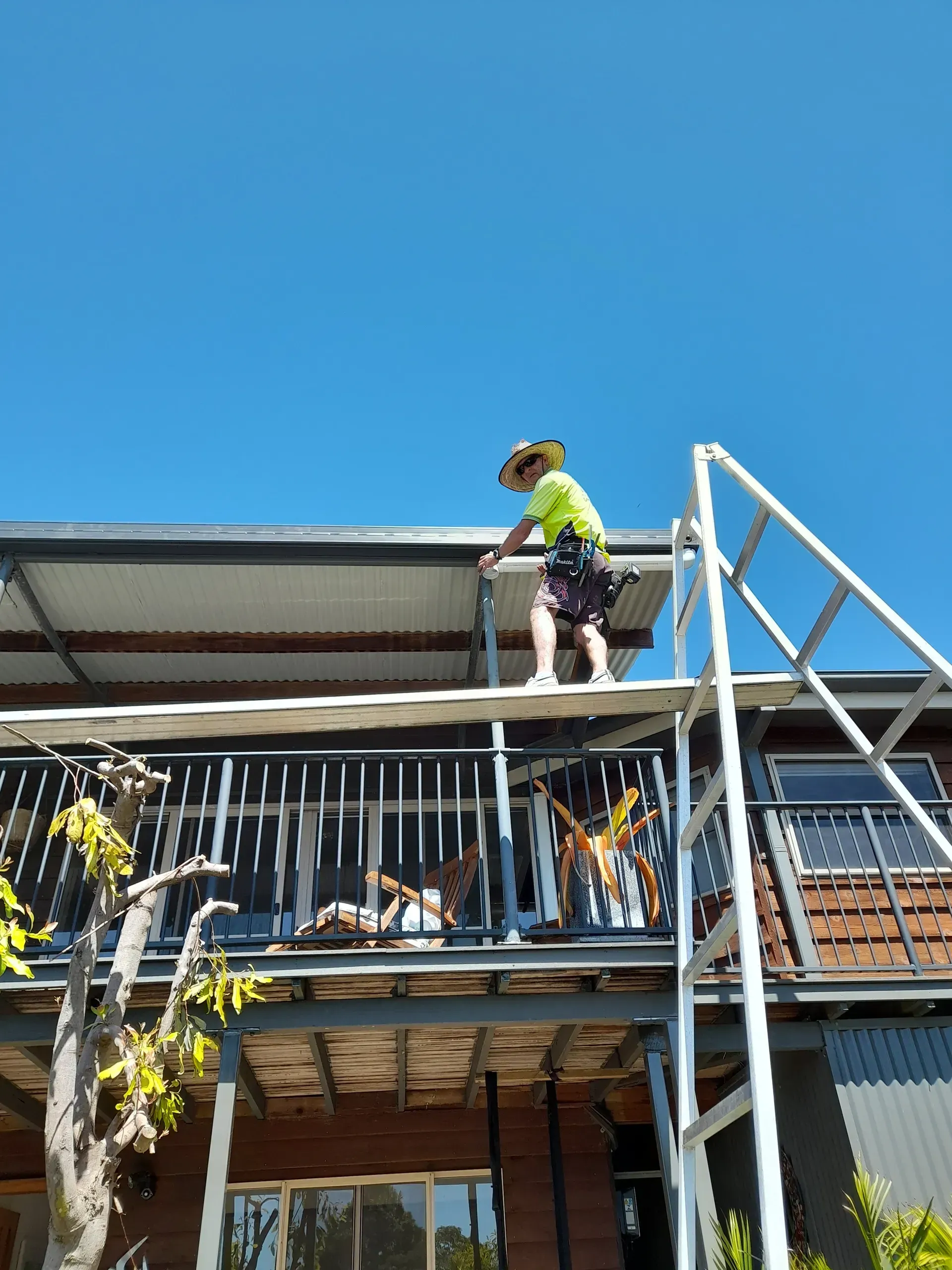 Person on scaffolding, working on a balcony roof under a blue sky.