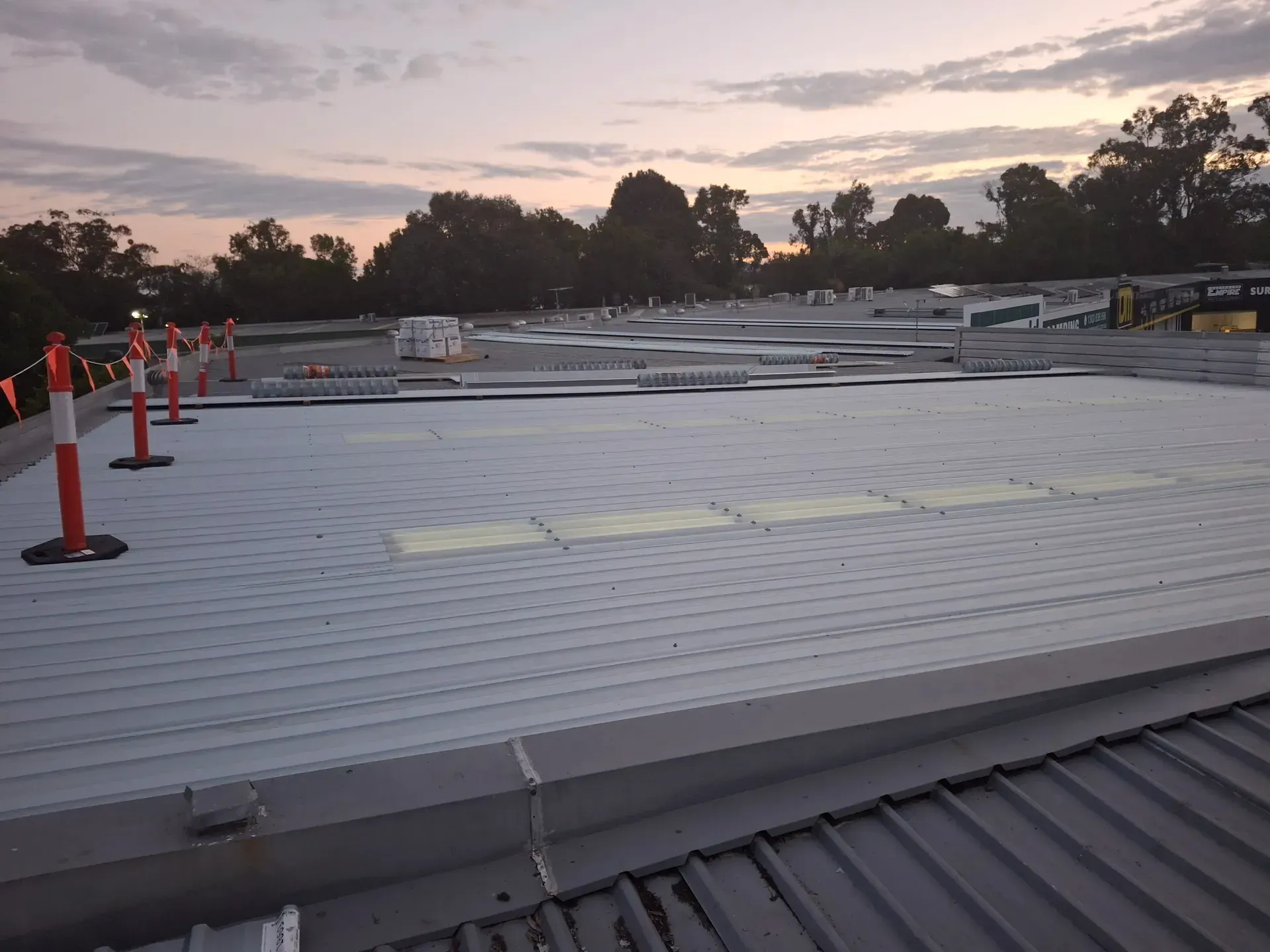 Flat roof construction site with safety cones and materials, dusk setting.