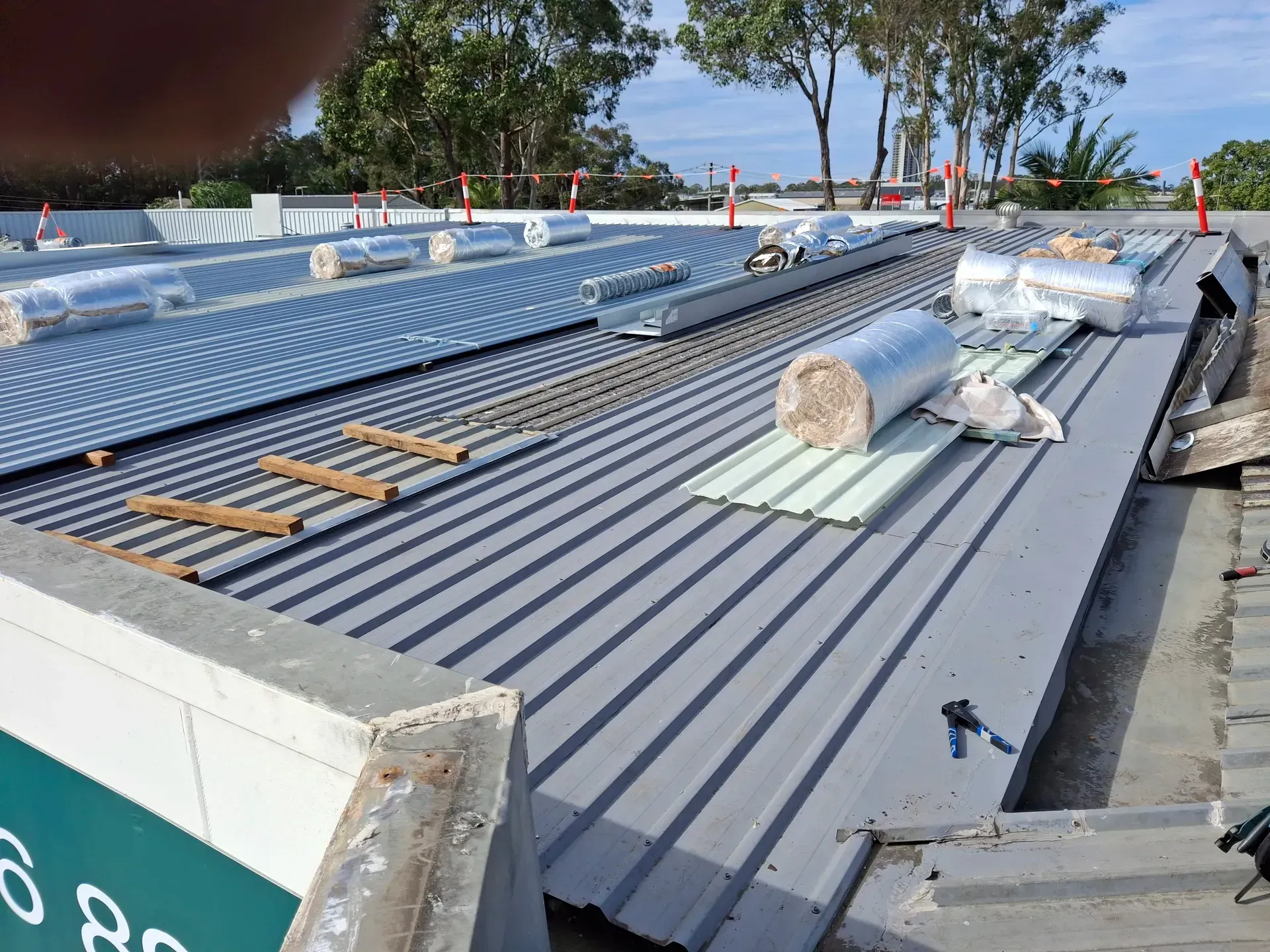 Metal roof under construction; rolls of insulation and panels on a flat roof.