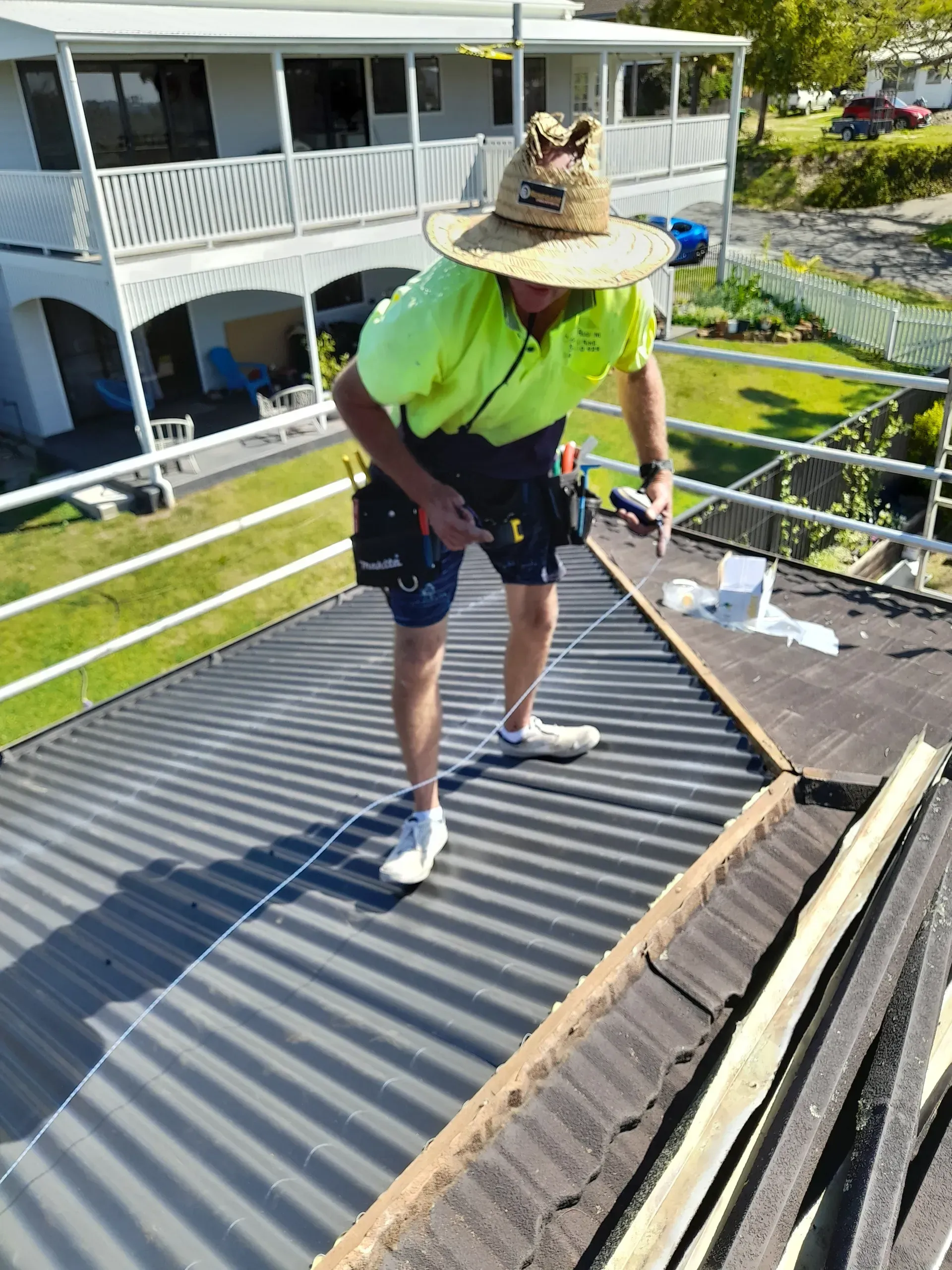 Person in safety gear on a roof, working. Wearing a hat and neon shirt. Sunny day.