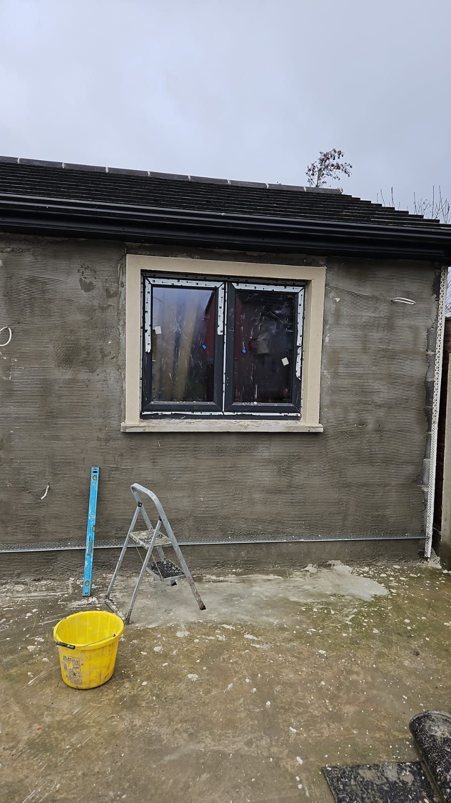 A yellow bucket is sitting in front of a brick building with a window.