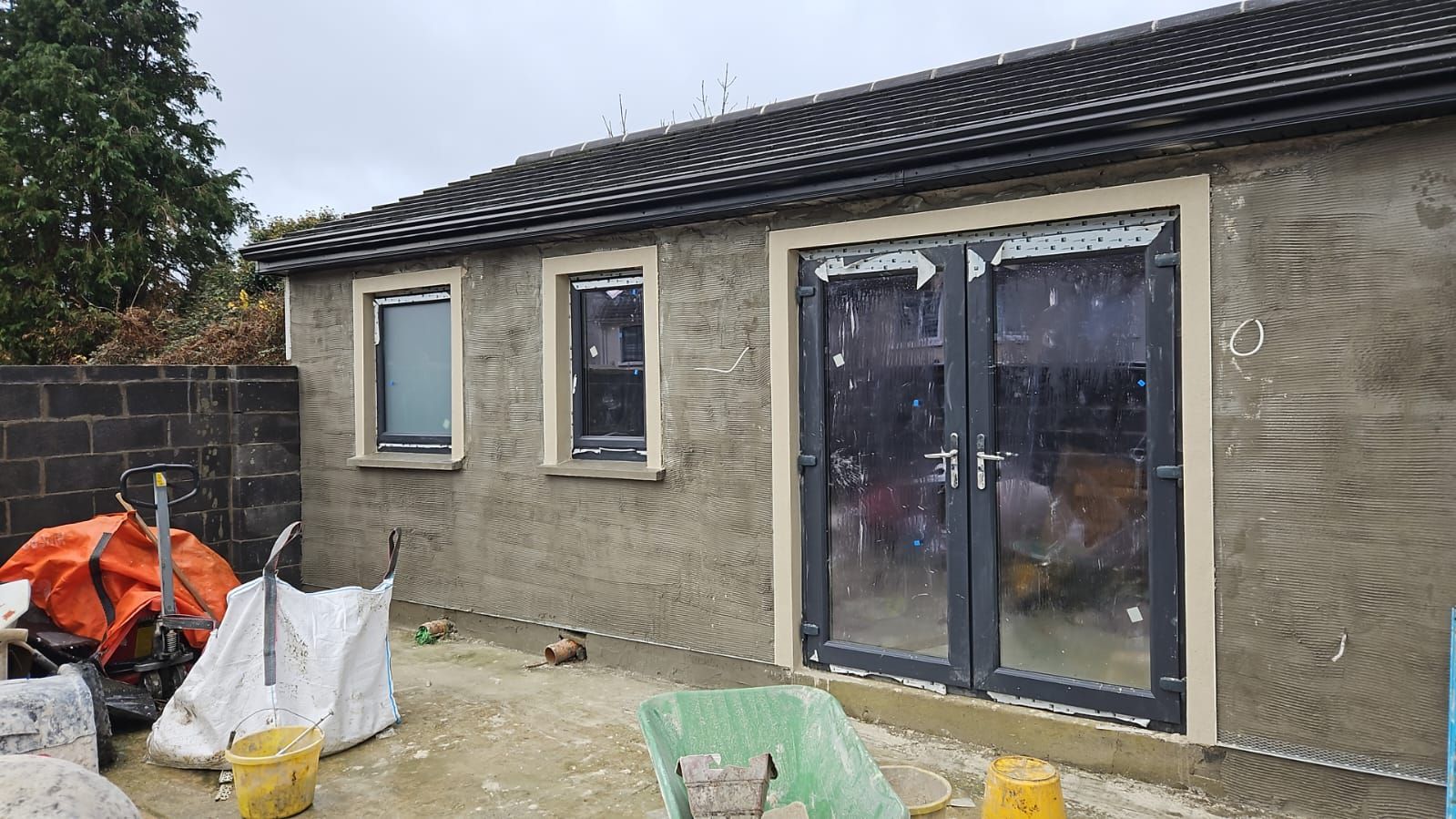 A building under construction with a green wheelbarrow in front of it.