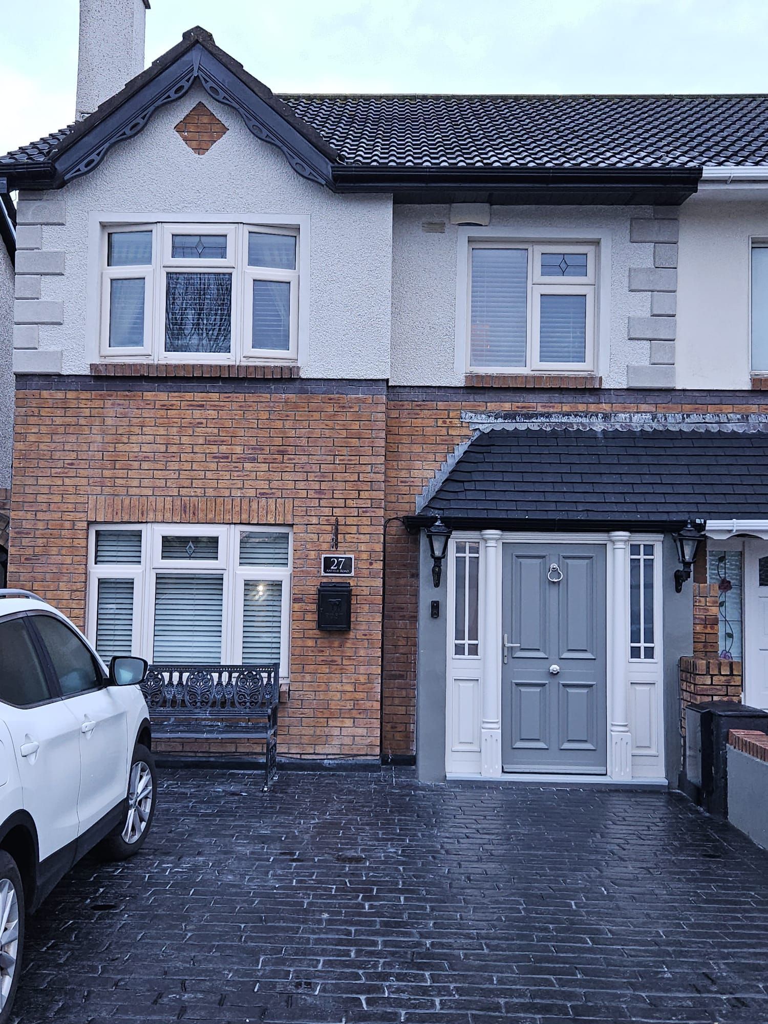 A white car is parked in front of a brick house.