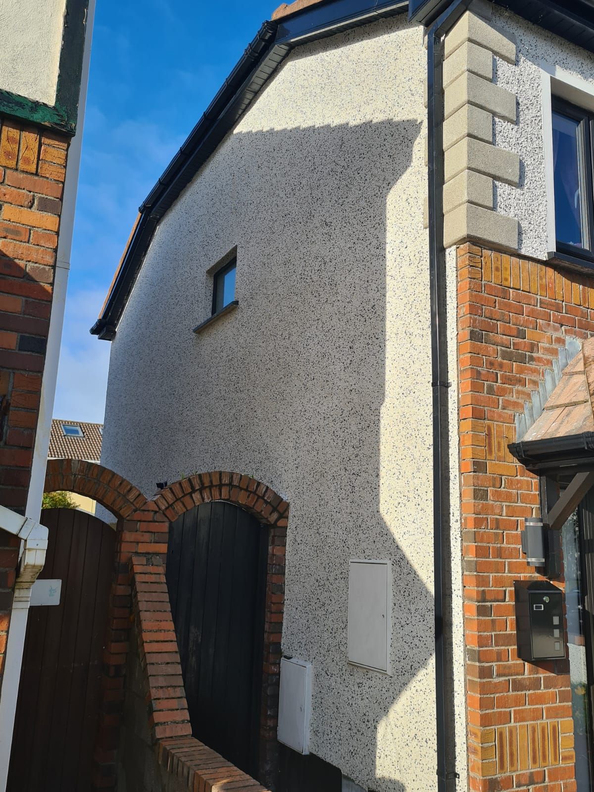 A white house with a brick wall and a black gutter.