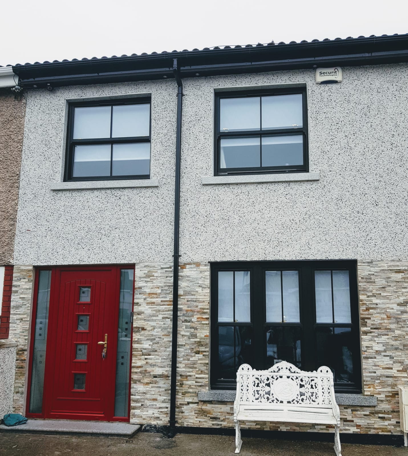 A white bench sits in front of a house with a red door