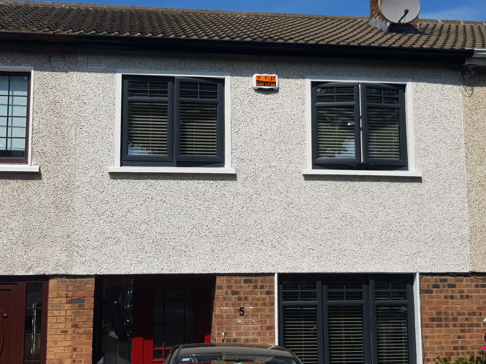 A car is parked in front of a house with a satellite dish on the roof.
