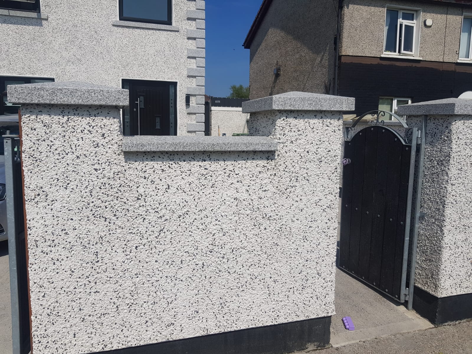 A white wall with a black gate in front of a house