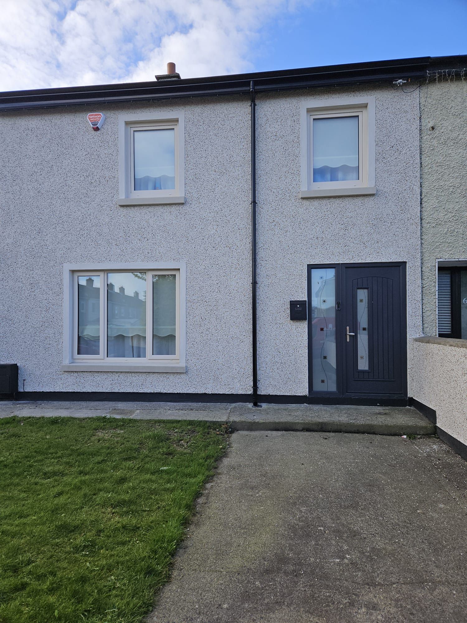 A white house with a black door and windows is sitting on top of a lush green lawn.