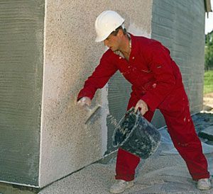 A man in a hard hat is plastering a wall with a trowel.