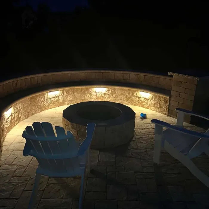 A fire pit is lit up at night and there are two chairs in front of it.