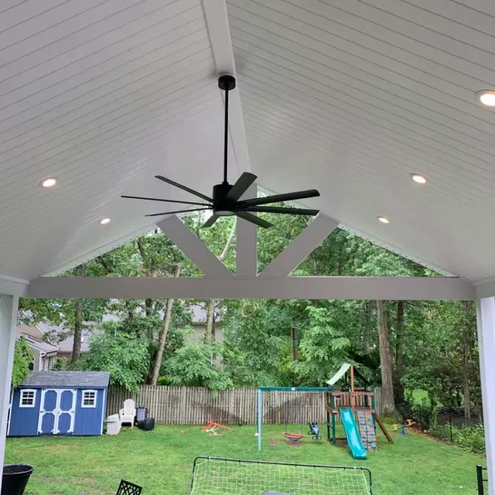 A ceiling fan is hanging from the ceiling of a covered patio.