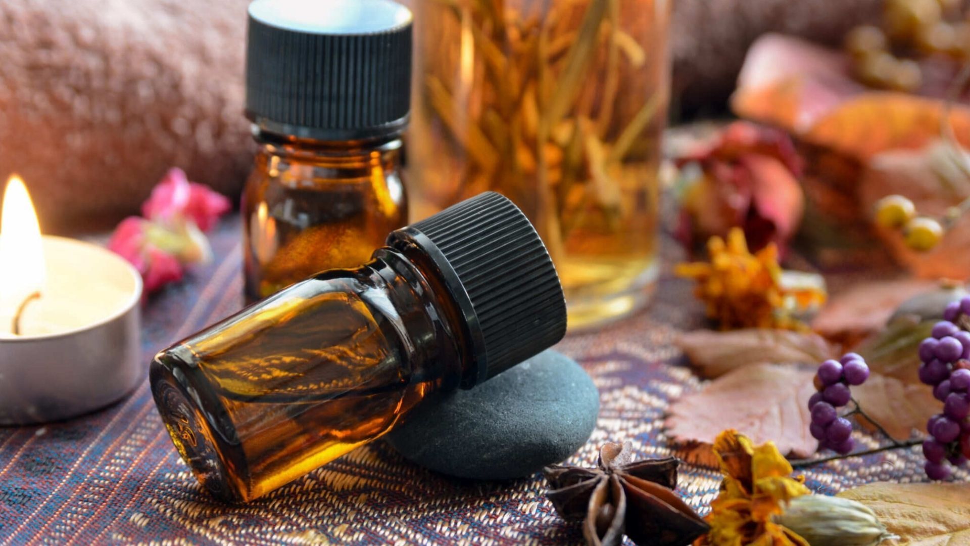 Amber essential oil bottles with a lit candle and decorative foliage.