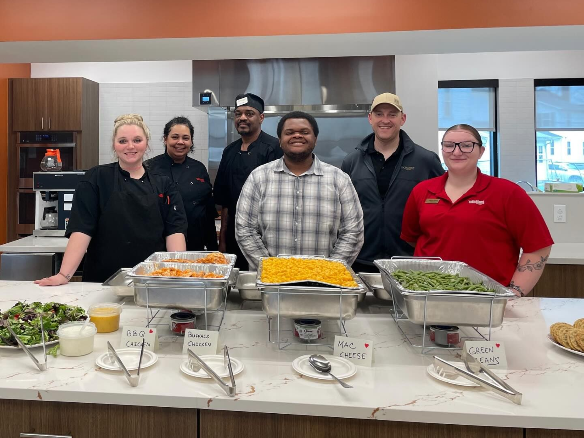 A group of people standing behind a buffet, smiling at the camera.