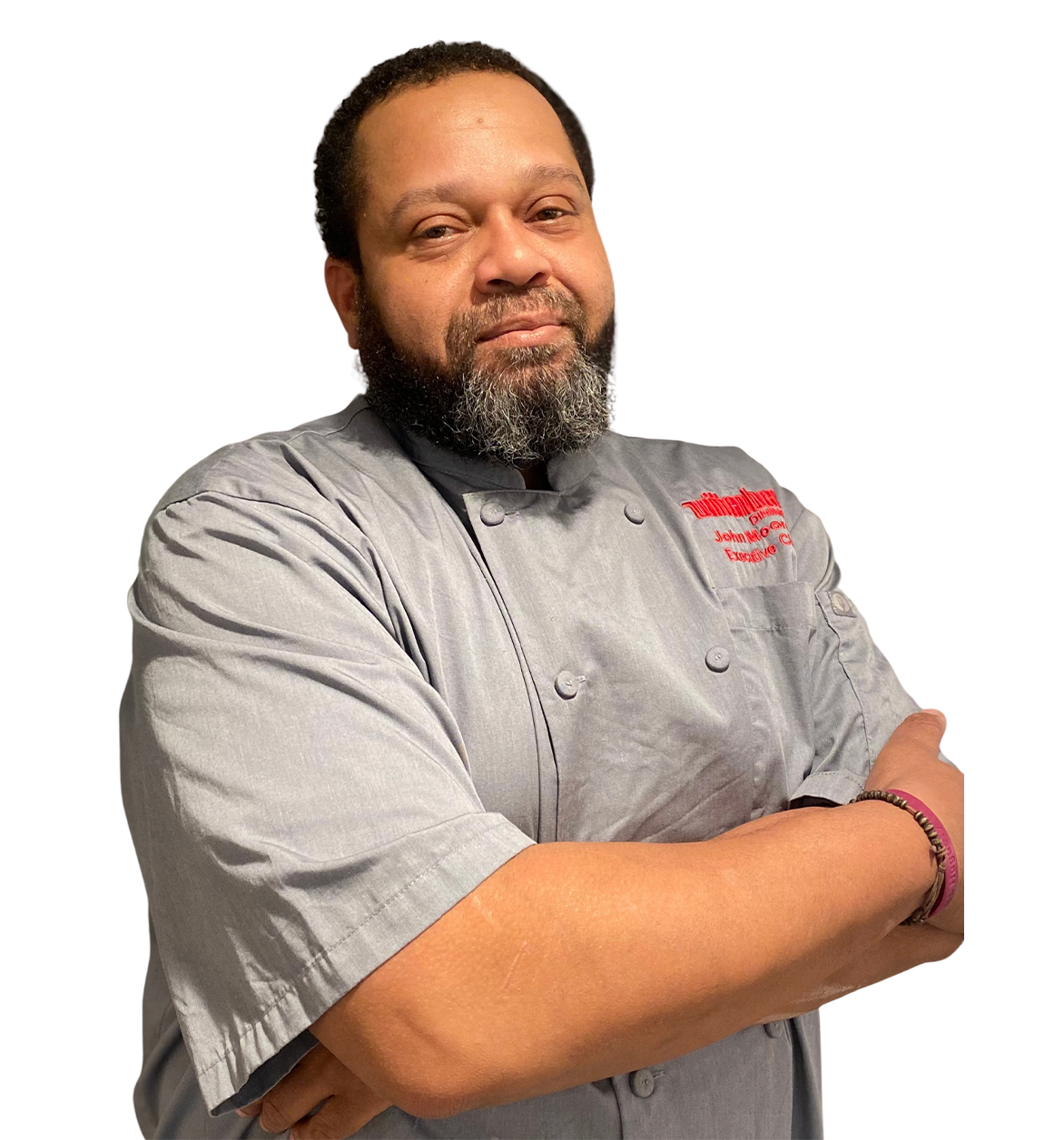 Chef in gray uniform with crossed arms, logo on shirt, looking at the camera.