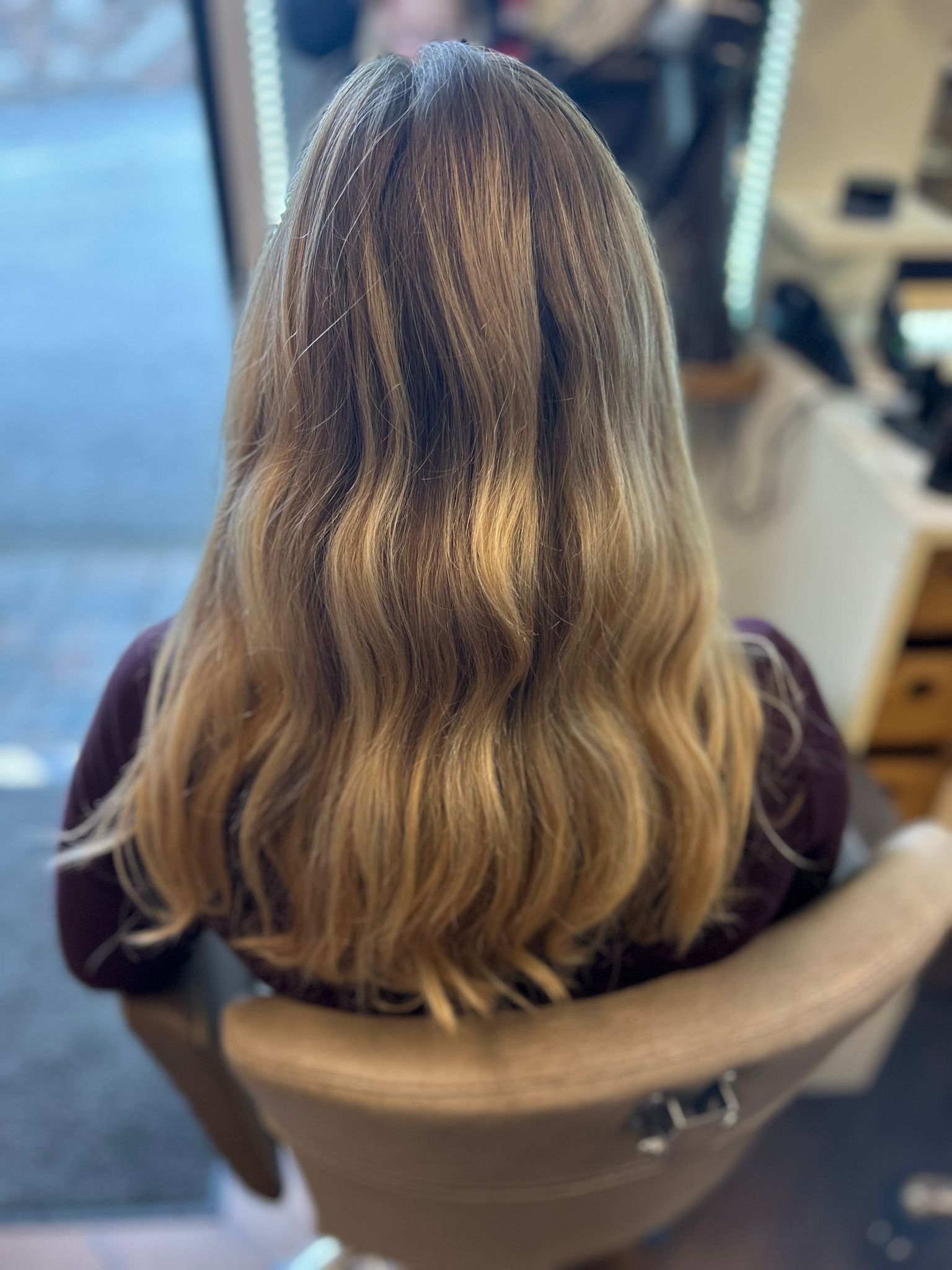 Frau mit hellbraunen Haaren sitzt auf einem Friseurstuhl und blickt in einen Spiegel.