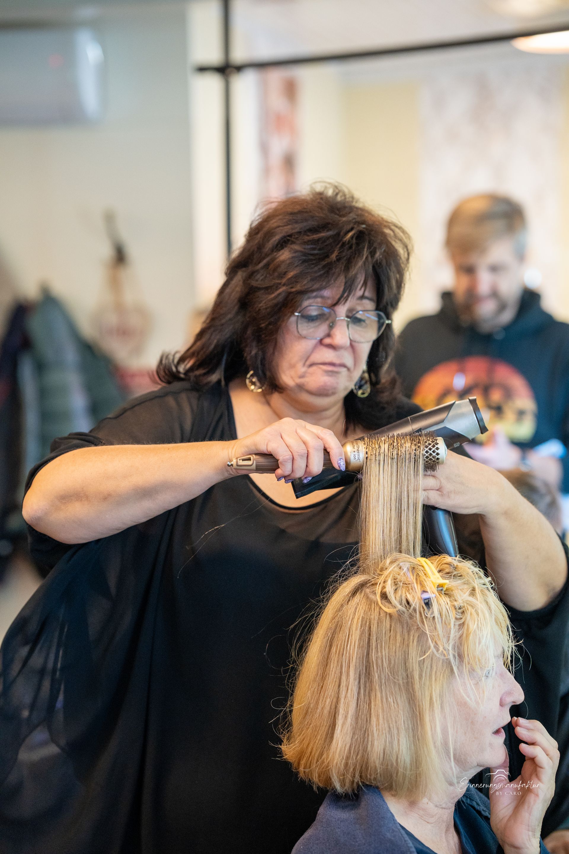 Eine Frau stylt in einem Salon die Haare einer anderen Frau mit einem Lockenstab