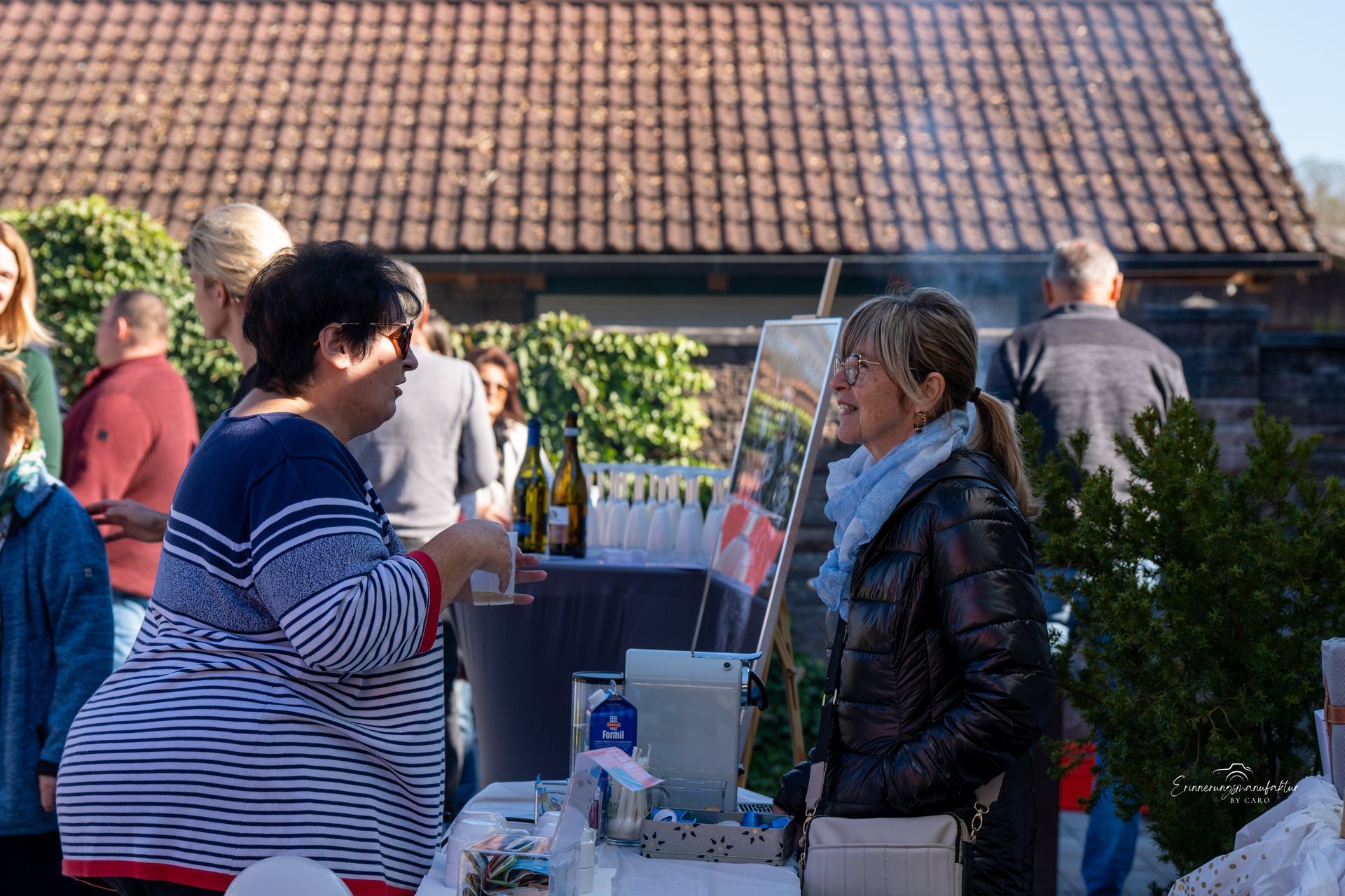 Menschen unterhalten sich bei einer Versammlung im Freien an einem Tisch mit Getränken vor einem Gebäude.