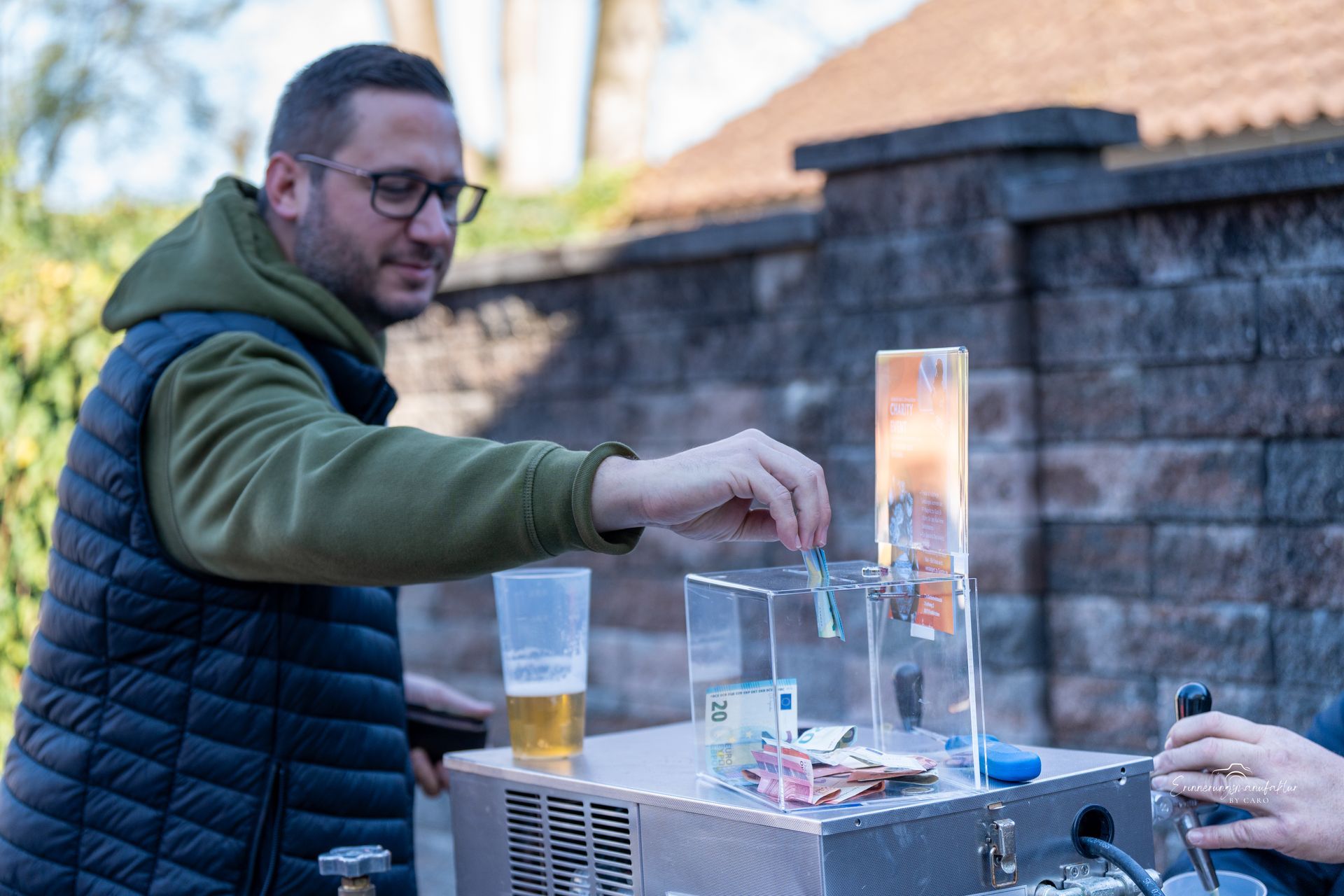 Ein Mann wirft Bargeld in eine Spendenbox in der Nähe eines Bierzapfhahns im Freien.