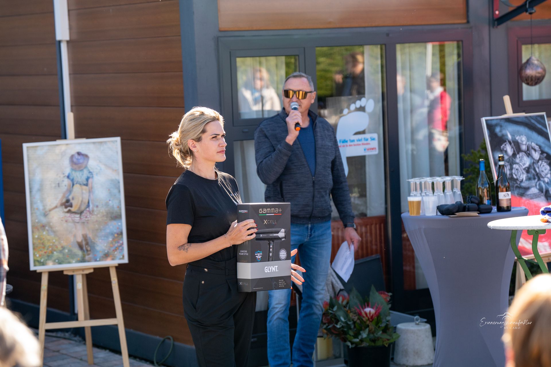 Eine Frau und ein Mann präsentieren bei einer Freiluftveranstaltung Kunst und einen Tisch.