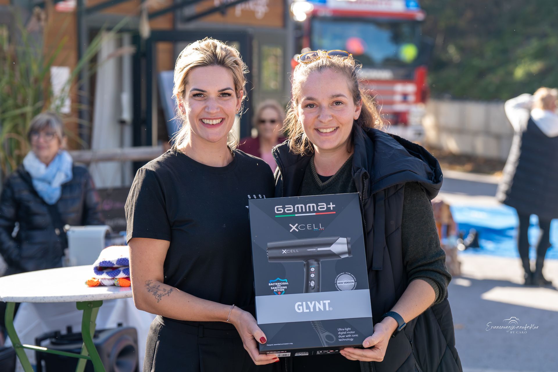 Zwei lächelnde Frauen halten im Freien eine Schachtel mit der Aufschrift „GLYNT“.