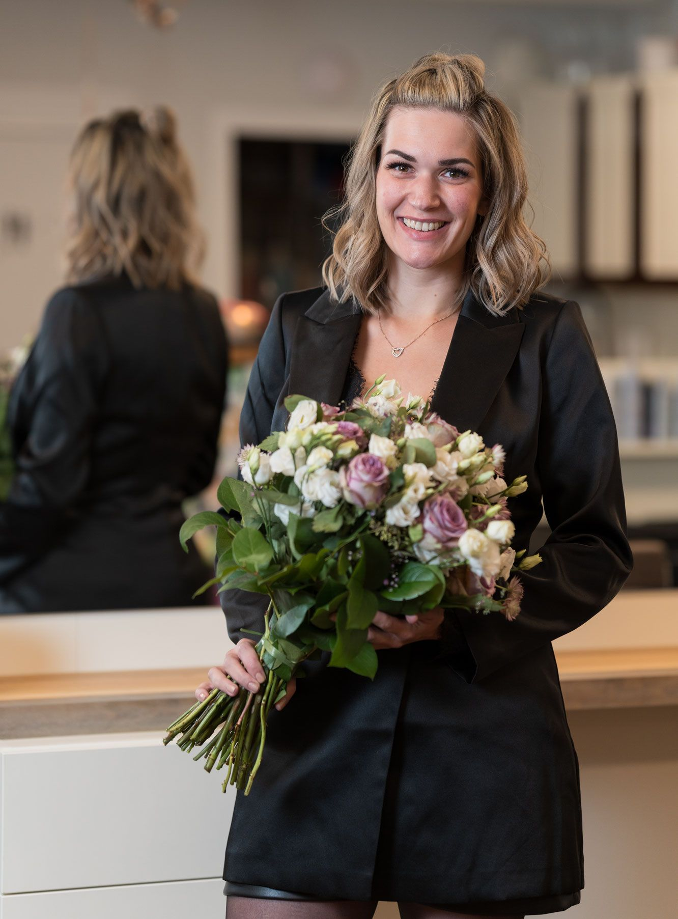 Frau in einem schwarzen Blazer, die einen Blumenstrauß hält und drinnen lächelt.