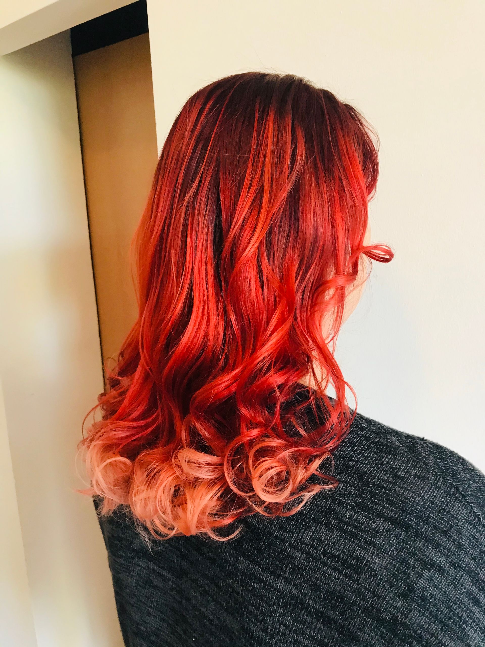 Frau mit gewelltem, rot-orangefarbenem Ombré-Haar, die einen grauen Pullover trägt.