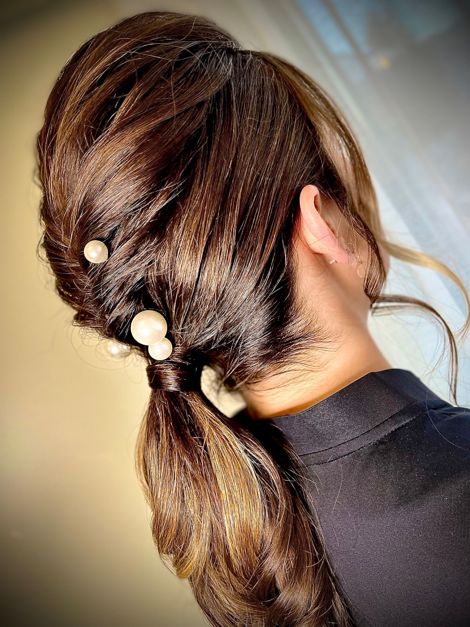 Frau mit dunkelbraunem Haar, das zu einem tiefen Pferdeschwanz gebunden ist und mit Perlenhaarnadeln geschmückt ist