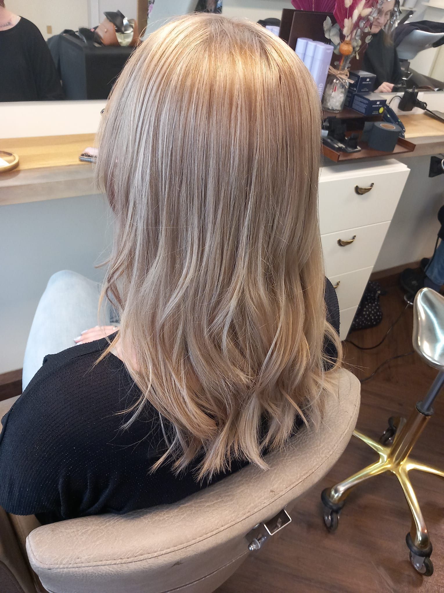 Frau mit blondem, gestuftem Haar sitzt auf einem Friseurstuhl und blickt in einen Spiegel.