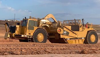 A large yellow bulldozer is sitting on top of a dirt field.