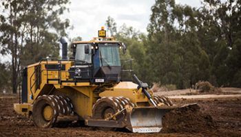 A yellow bulldozer is driving through a dirt field.