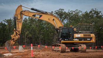 A large yellow excavator is sitting on top of a dirt field.