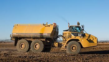 A yellow dump truck is driving through a muddy field.