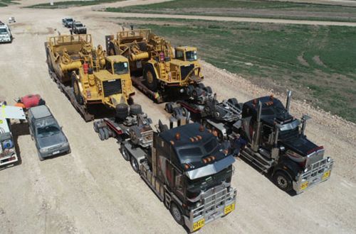A group of trucks are driving down a dirt road.