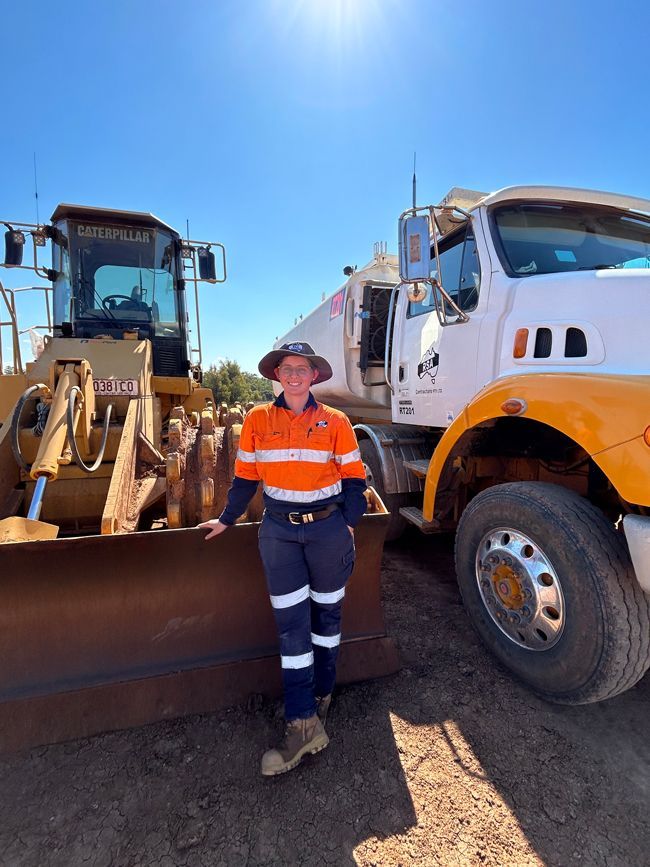 A woman is standing next to a bulldozer and a truck.