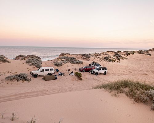 A group of cars are parked on a sandy beach near the ocean.
