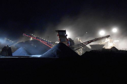A large pile of coal is being processed in a factory at night.