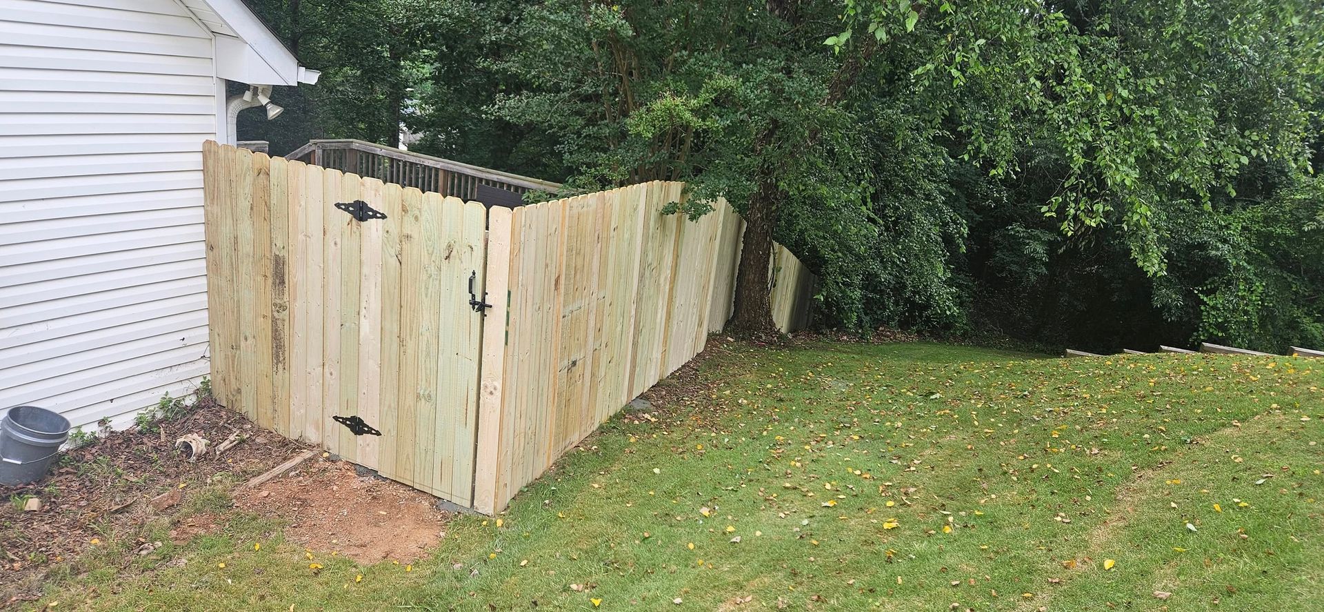Wooden fence surrounding an outdoor utility area next to a house. Green grass and bushes are also present.