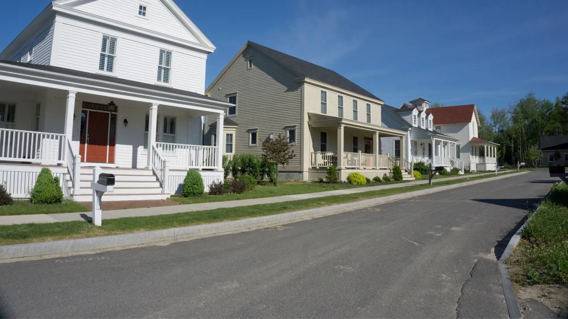 Row of houses along a street on a sunny day. White, tan, and red exterior colors are visible.